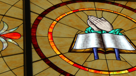 Stained Glass Window with Open Book and Hands in Prayer