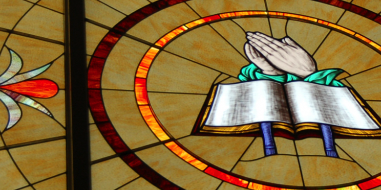 Stained Glass Window with Open Book and Hands in Prayer