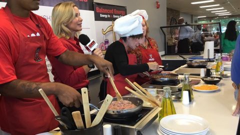 Three Chefs Working Behind Counter While Reporter Talks on Microphone