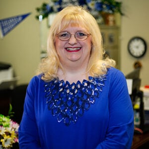 Woman with light blonde hair smiling into camera wearing royal blue shirt.