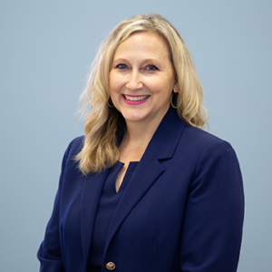 A woman with mid length blonde hair is wearing a navy blue suit while smiling into the camera.