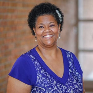 Woman with short dark hair smiling into camera wearing a blue floral shirt.