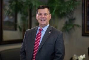 Man in dark suit with red tie smiling into camera.