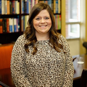 Woman with long brunette hair wearing cheetah print shirt and smiling.