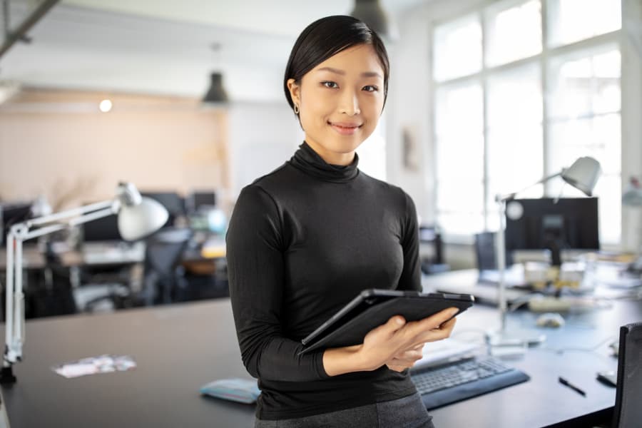 A woman in all black clothing holding an ipad and smiling