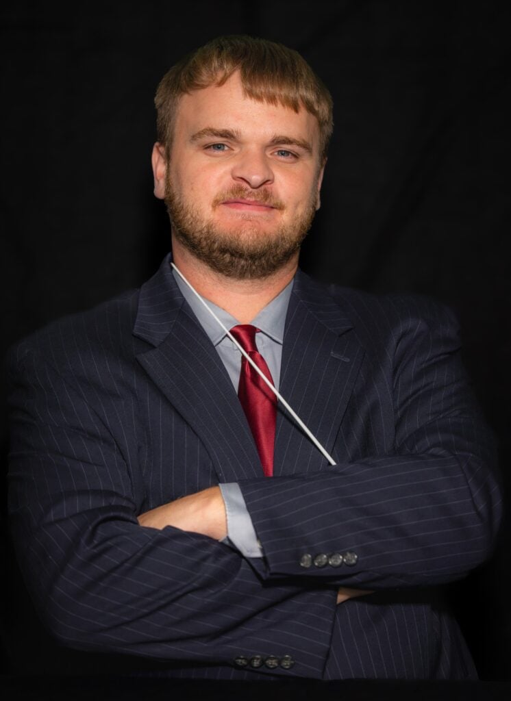 Josh Guy, wearing a suit, poses with arms folded in front.