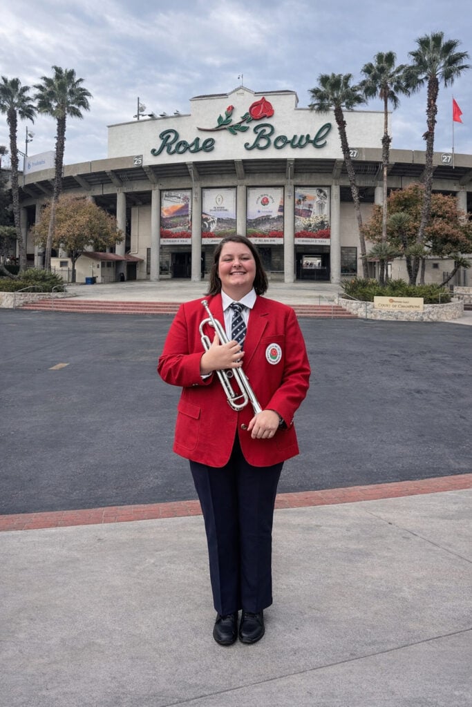 Rebecca Potter stands in front of The Rose Bowl holding her trumpet.