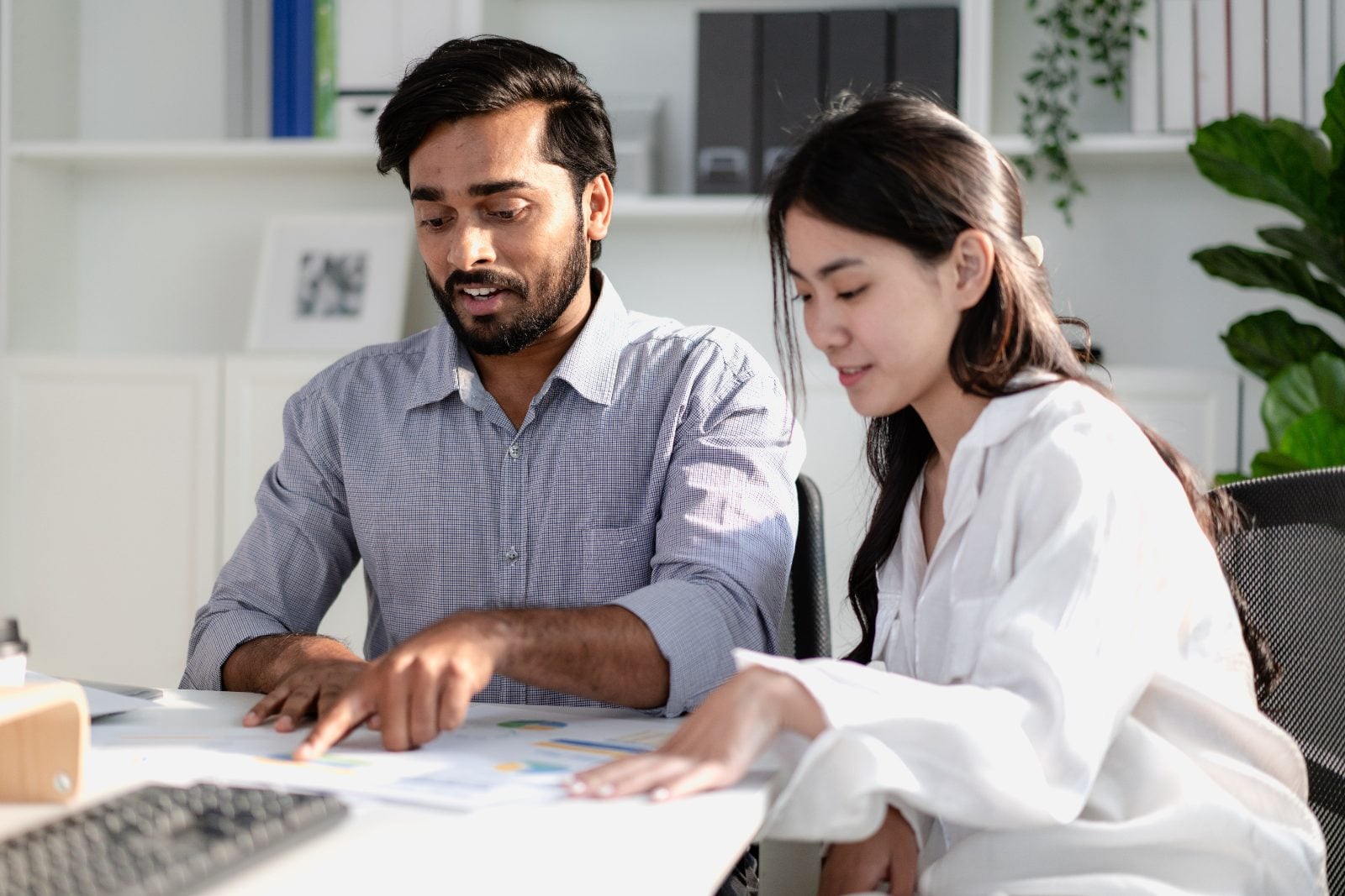Two doctoral students reviewing printed charts and research data together at a desk