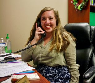 Smiling Woman on Phone Behind Desk Posing for Photo