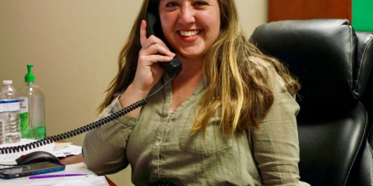 Smiling Woman on Phone Behind Desk Posing for Photo