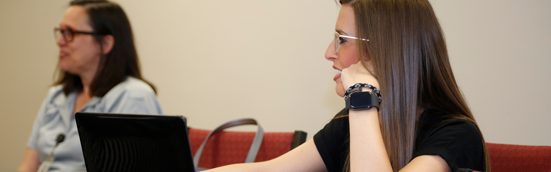 Two adult students watch class lecture while taking notes on a laptop