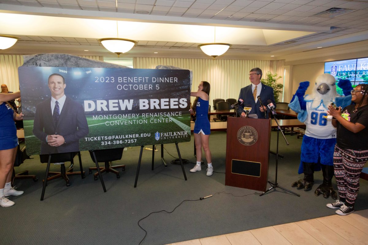Faulkner University President Mitch Henry announces Drew Brees as the university's 2023 Benefit Dinner speaker as two members of the Faulkner Cheer team unveil the promotional billboard.