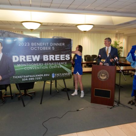 Faulkner University President Mitch Henry announces Drew Brees as the university's 2023 Benefit Dinner speaker as two members of the Faulkner Cheer team unveil the promotional billboard.