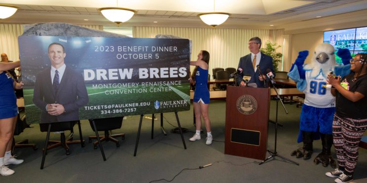 Faulkner University President Mitch Henry announces Drew Brees as the university's 2023 Benefit Dinner speaker as two members of the Faulkner Cheer team unveil the promotional billboard.