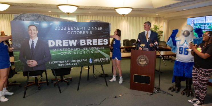Faulkner University President Mitch Henry announces Drew Brees as the university's 2023 Benefit Dinner speaker as two members of the Faulkner Cheer team unveil the promotional billboard.