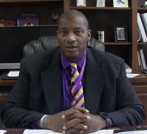 Dr. Gregory Moore sits behind his desk with his hands folded in front of him. 