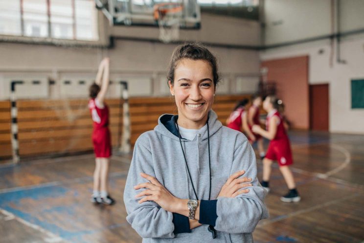 A young coach smiles for the camera while her basketball team practices