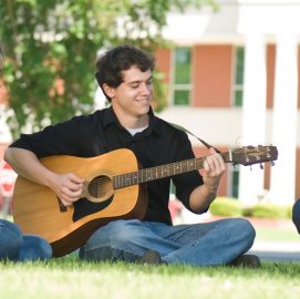 Aaron Reynolds plays his guitar in front of the Harris College of Business.