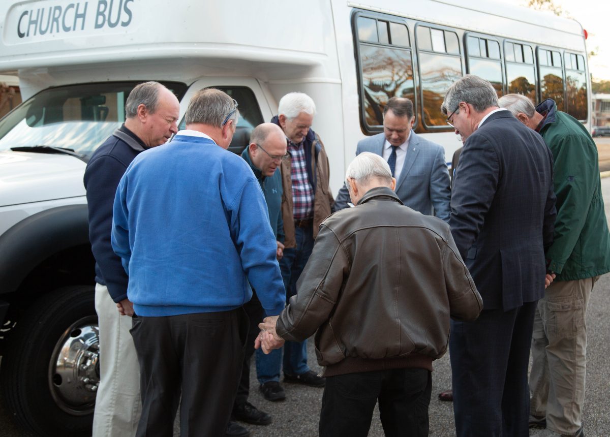 Elders of Dalraida Church of Christ and leaders from Faulkner University hold hands as they pray over the new bus being donated to Faulkner in the parking lot of the church.