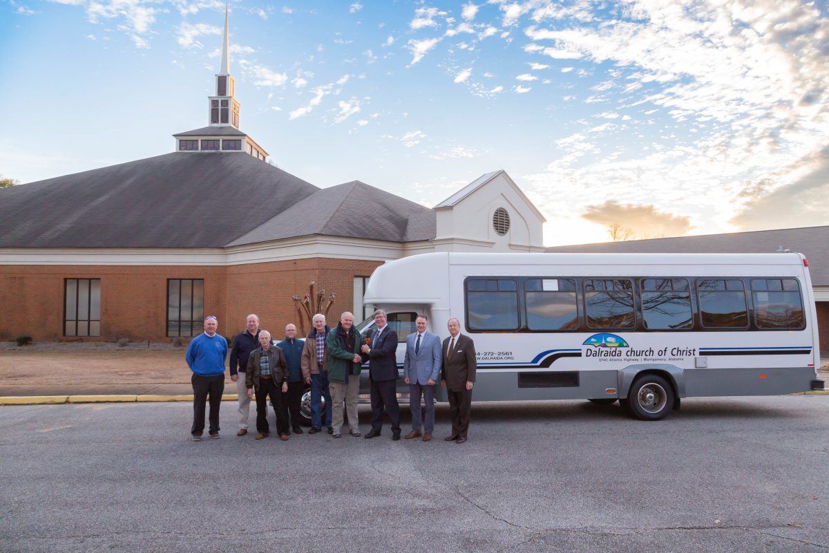 Elders of Dalraida Church of Christ and leaders from Faulkner University post in front of the newly donated bus in front of the church in the parking lot. 