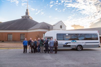 Elders of Dalraida Church of Christ and leaders from Faulkner University post in front of the newly donated bus in front of the church in the parking lot.