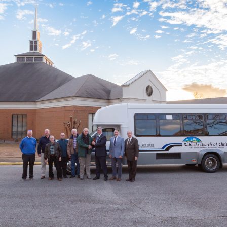 Elders of Dalraida Church of Christ and leaders from Faulkner University post in front of the newly donated bus in front of the church in the parking lot.