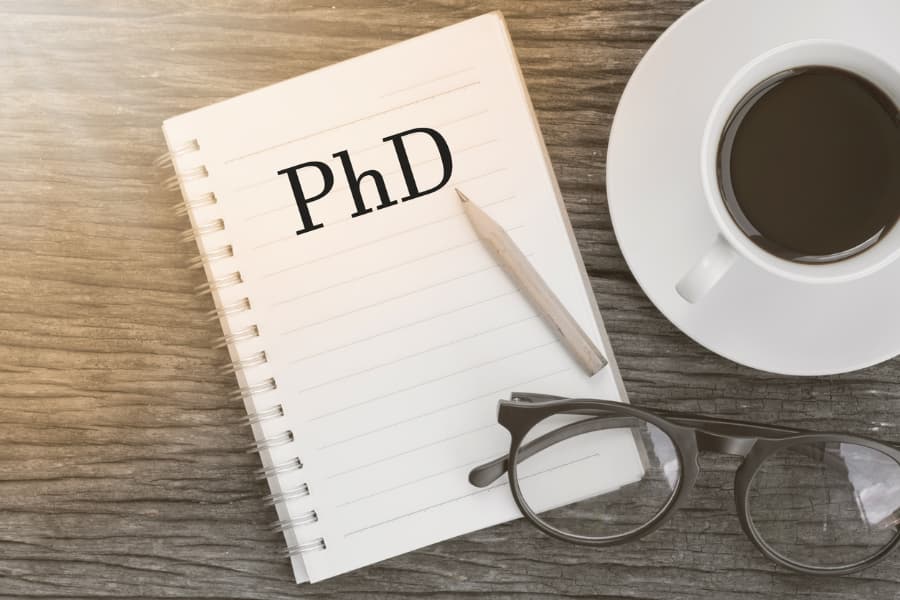 Illustration of coffee cup, glasses, and notebook with “PhD” typed on it