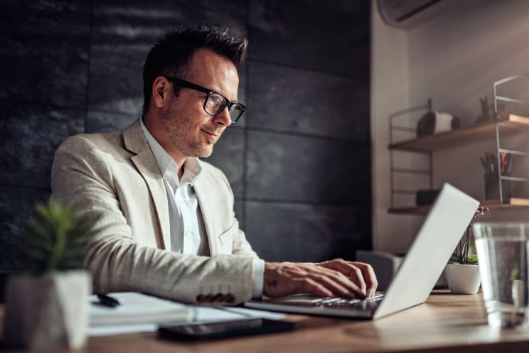 Graduate student in blazer and glasses working on laptop at desk