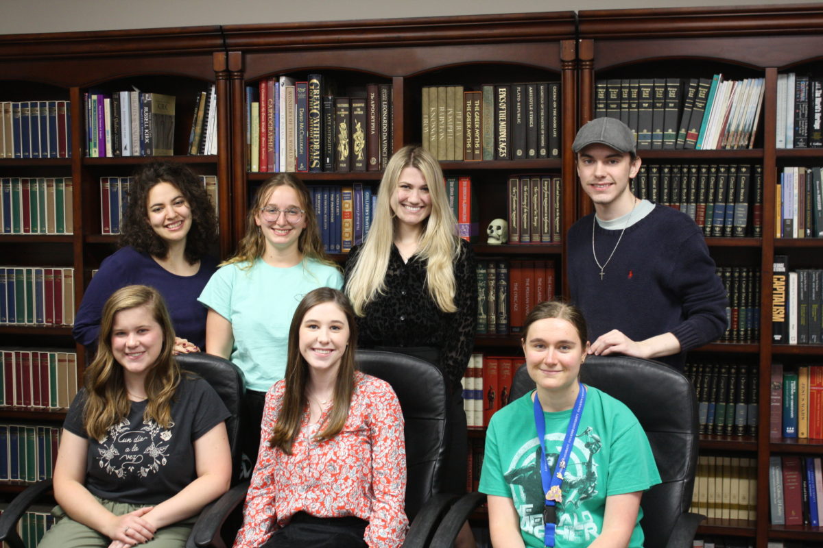 l-r back row Nicolette Connelly, Katelyn Lape, Emma Revels, Benjamin Tomlin. l-r front row Abigail Sikes, Madelyn Furlong, Crystal Klose are a part of the Great Books Council. They post seated and standing in front of a wall of books.  
