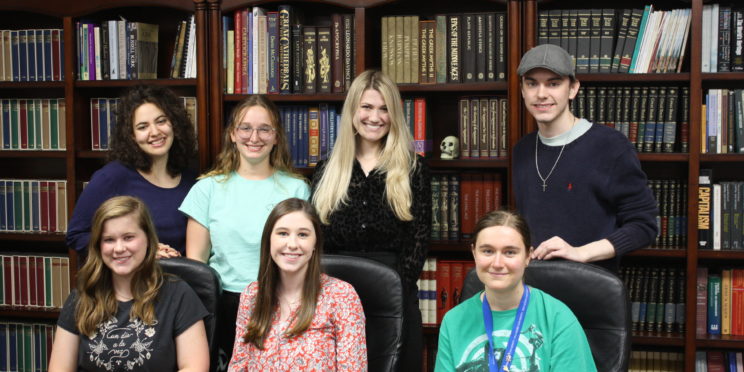 l-r back row Nicolette Connelly, Katelyn Lape, Emma Revels, Benjamin Tomlin. l-r front row Abigail Sikes, Madelyn Furlong, Crystal Klose are a part of the Great Books Council. They post seated and standing in front of a wall of books.