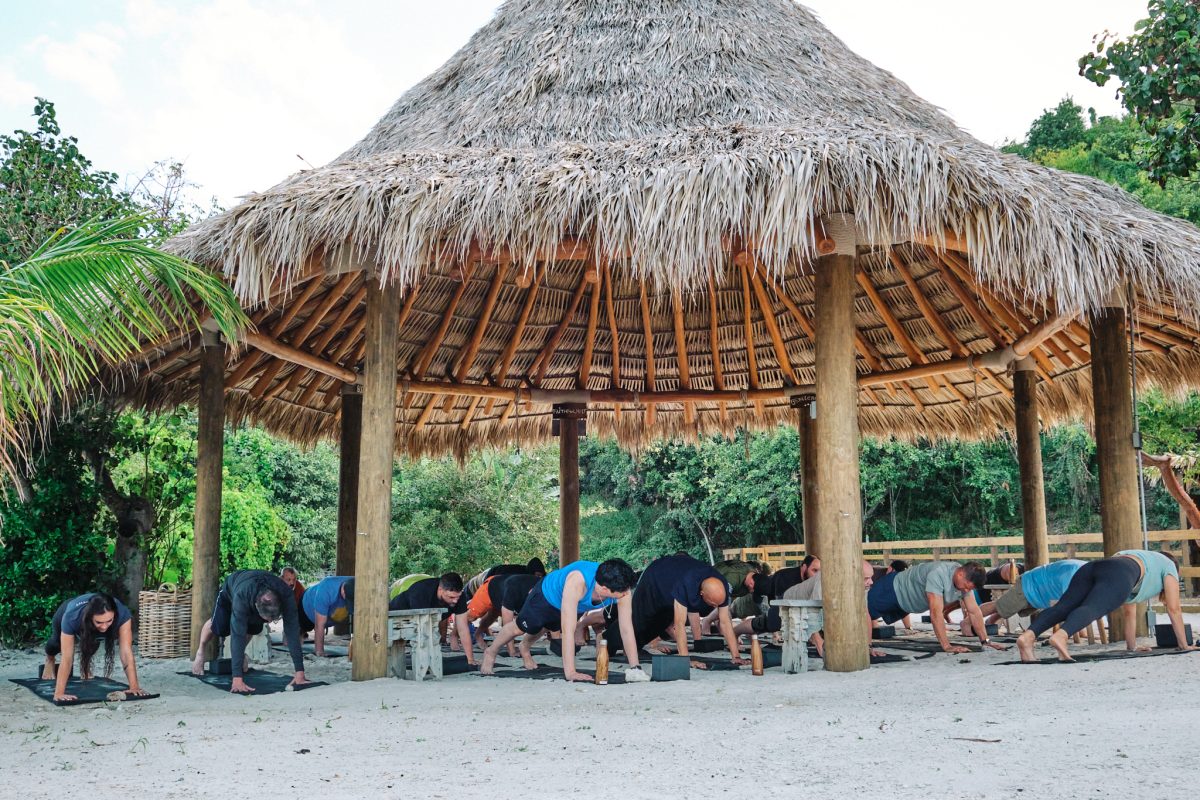 Participants with Heal the Heroes take part in a healing yoga session under a thatched roof hut. 