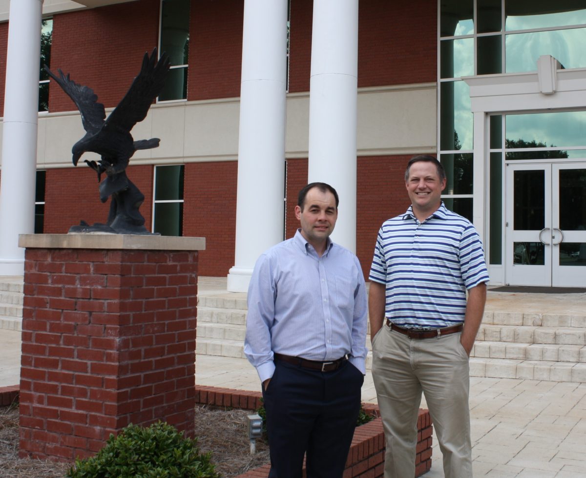 l-r William Cooper and Justin Boyd pose in front of the Harris College of Business building next to a bronzed eagle. They are pursuing their PhDs. 