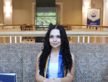 Sinclair Drysdale sits on a couch with her graduation stole and cords.