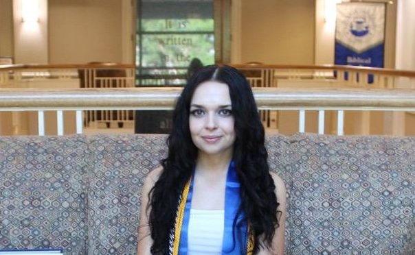 Sinclair Drysdale sits on a couch with her graduation stole and cords.