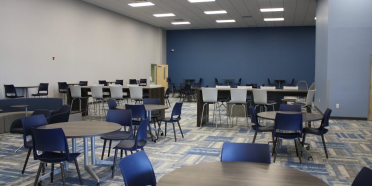 Renovations of the College of Health Sciences include blue painted walls, blue and gray patterned carpeting and tables and chairs in the lobby area.