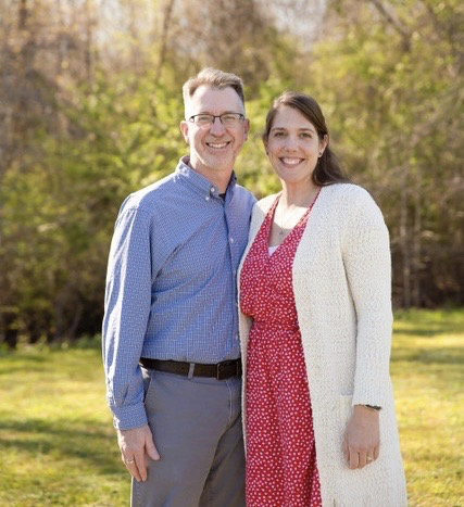 Jason Owen and his wife Celia pose together outside against a backdrop of trees. 