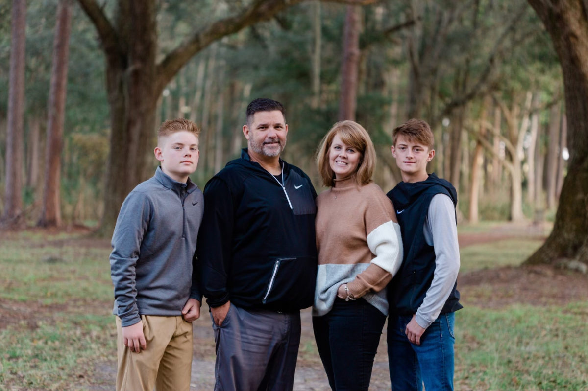 Chuck Knapp and his wife, Julie Knapp pose with their two sons in the middle of the woods. 