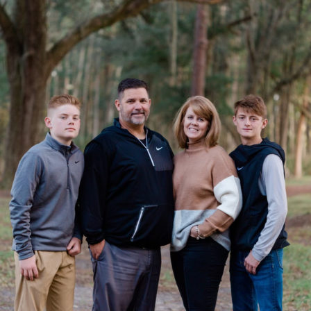 Chuck Knapp and his wife, Julie Knapp pose with their two sons in the middle of the woods.