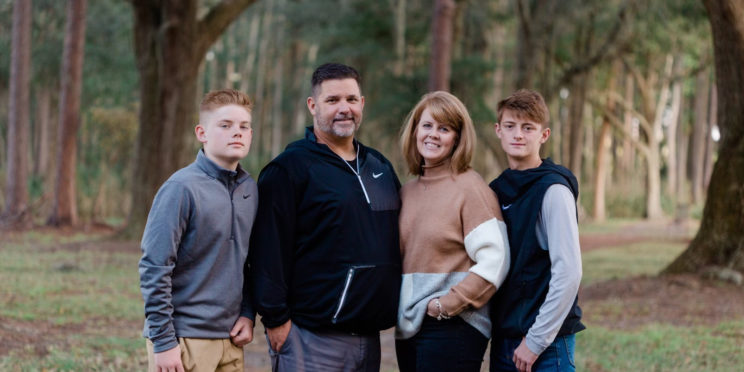 Chuck Knapp and his wife, Julie Knapp pose with their two sons in the middle of the woods.