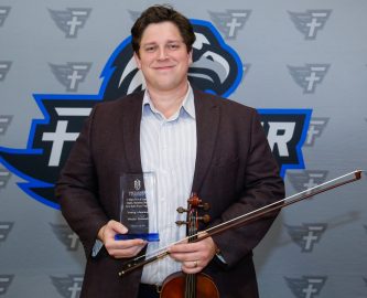 Westley Schlundt holds his violin and award. As a musician, he was honored as the Faulkner Young Alumnus for the Music Department.