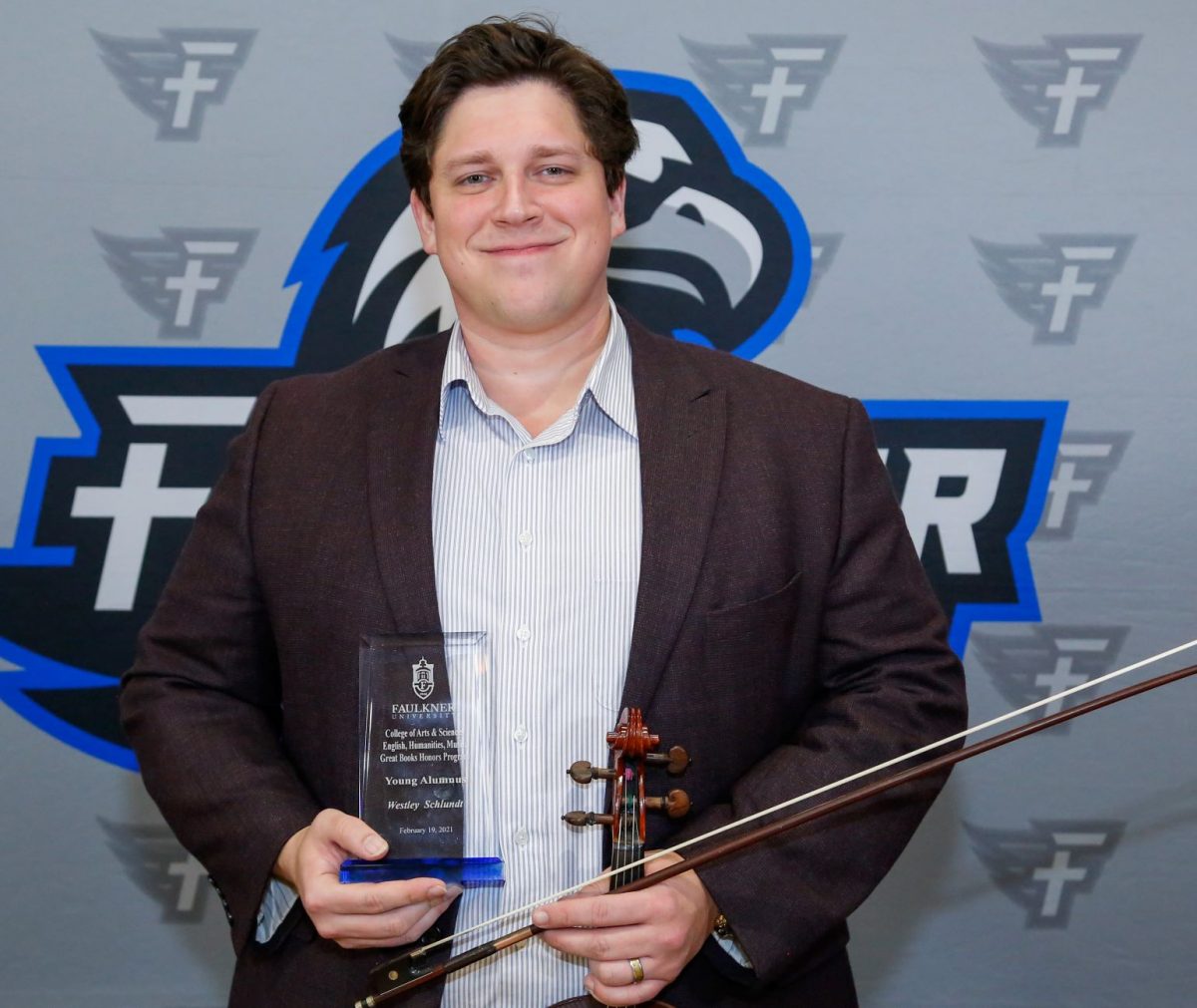 Westley Schlundt holds his violin and award. As a musician, he was honored as the Faulkner Young Alumnus for the Music Department.