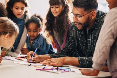 Male teacher sitting with elementary students and drawing