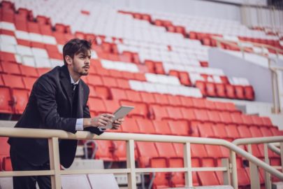 Man holding tablet standing in stadium looking out over field