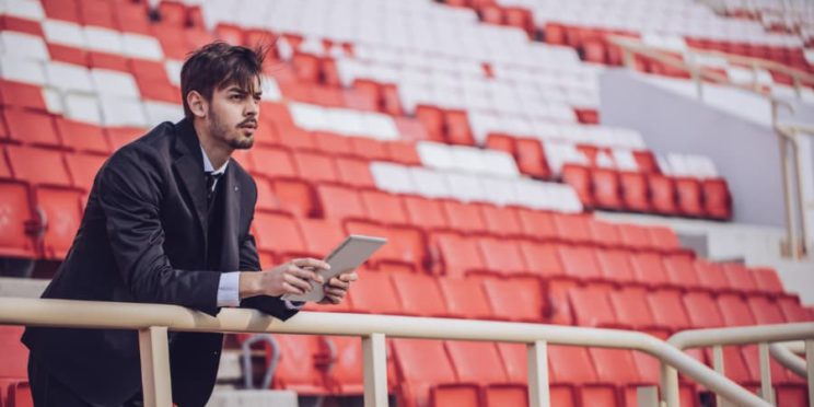 Man holding tablet standing in stadium looking out over field