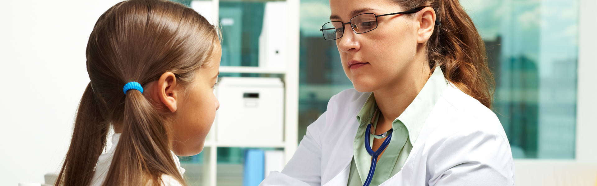 Physician assistant in white coat wearing stethoscope and examining pediatric patient