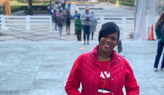 Judge Ruby Davis stands outside in a red coat and a t-shirt with her slogan.