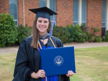 Kelli Stewart Mallett wears her graduation cap and gown while holding her diploma. 