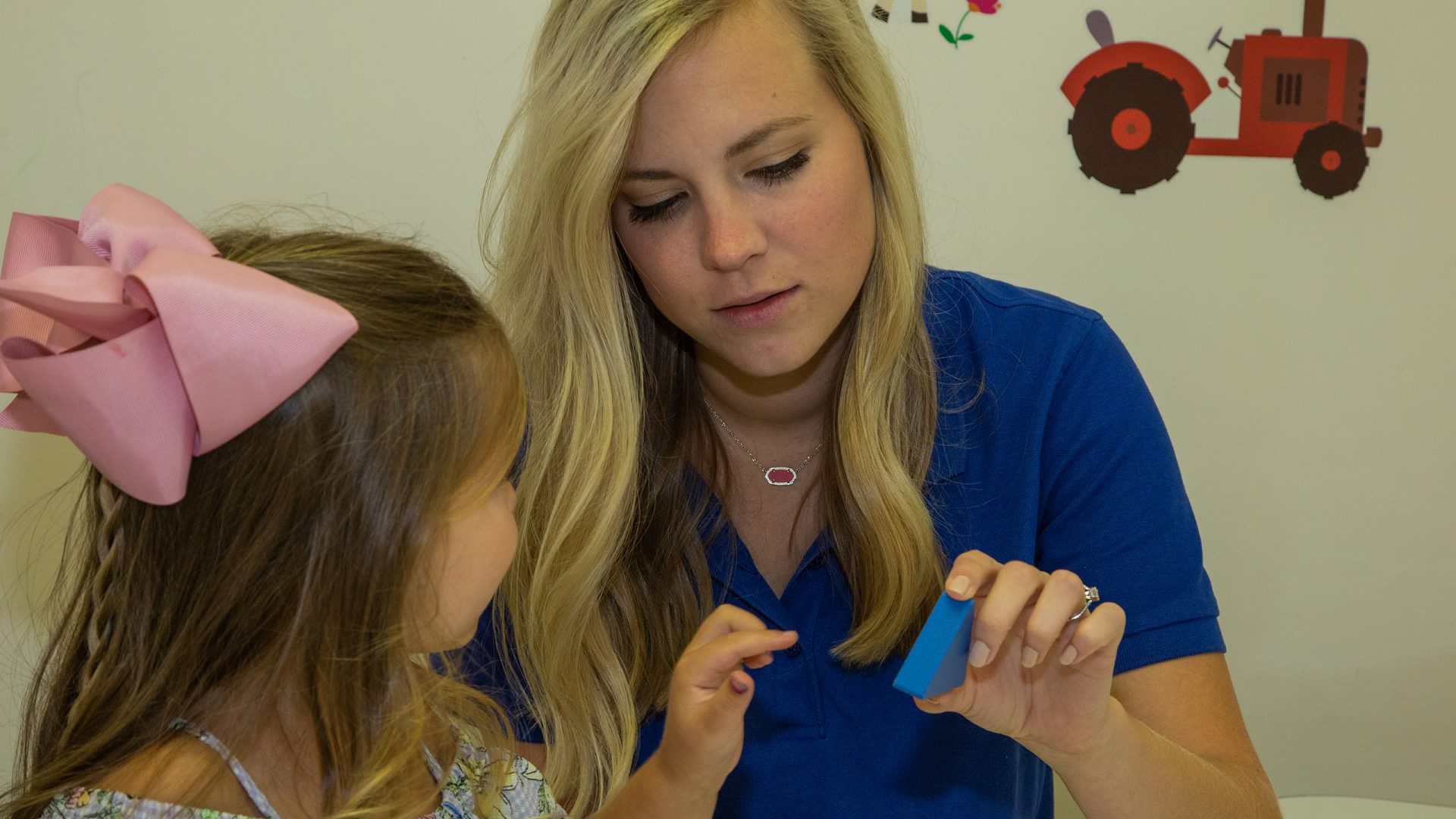 Speech-language pathologist showing blue triangle to child wearing pink bow