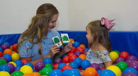 Pathologist playing in ball pit holding up flash cards to child