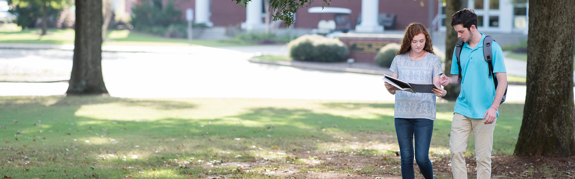 Two Faulkner University students walking outside looking at a notebook